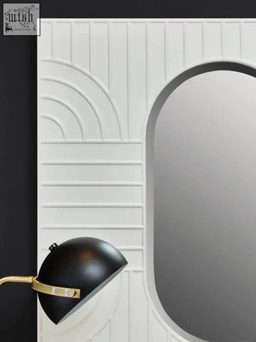 A sleek black dome lamp with gold accent next to a danta off-white wall mirror in an off-white wall panel