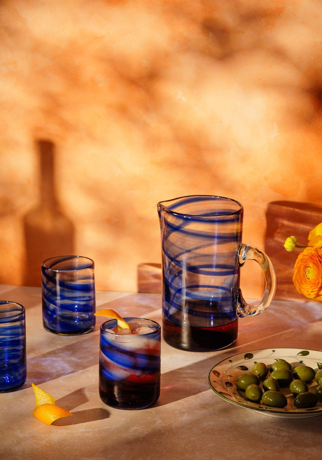 Blue glass daphne jug with swirling patterns and handle filled with dark liquid perfect for serving drinks