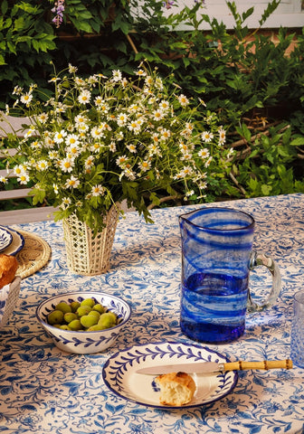 A vibrant blue glass daphne jug with swirling patterns and a sturdy handle sits on a table
