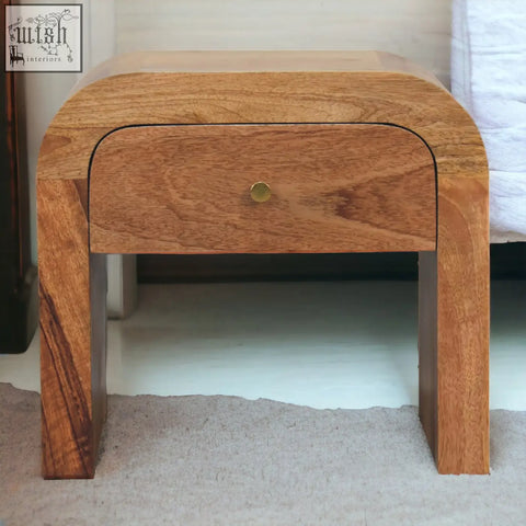 A sleek curved solid mango wood darcy bedside table with a single drawer and brass round knob