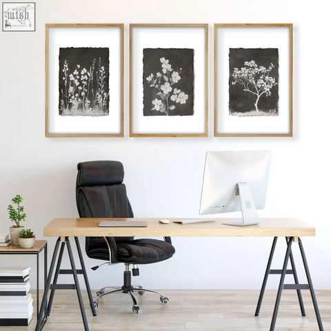 Set of three brown wall art prints featuring white floral and tree silhouettes on dark textured paper in light wood frames