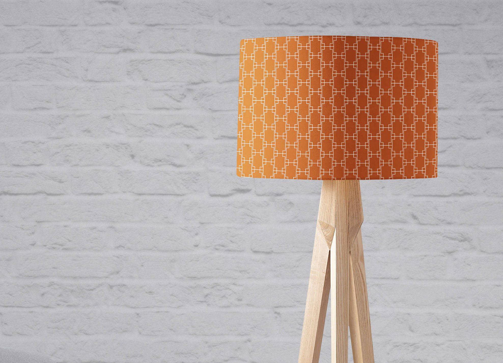 Dark orange table lamp with white geometric design on orange lampshade and light wood tripod base