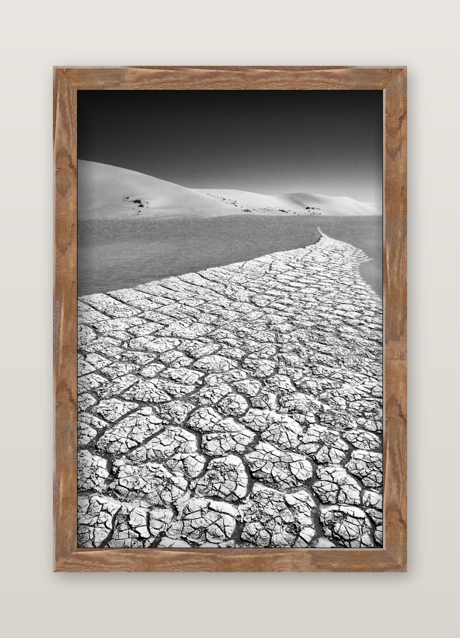 A fine art black and white photograph by david ballam showing cracked dry earth and sand dunes under a gradient sky