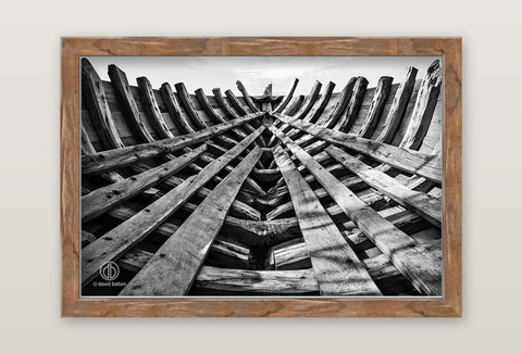 A rustic wooden-frame black-and-white fine art photo by david ballam showing a boat interior framework under construction