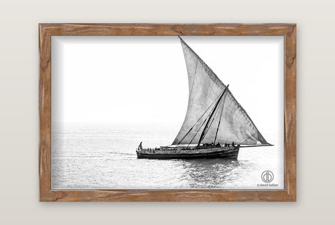 A black-and-white framed fine art photo by david ballam of a traditional wooden sailboat with a single sail on calm water