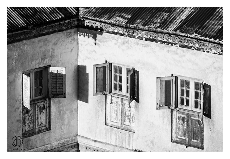 Fine art image by david ballam showing weathered wooden windows with dark shutters in a textured aged wall