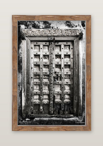 Black and white fine art photo by david ballam of an intricately carved wooden door with ornate floral detailing above frame