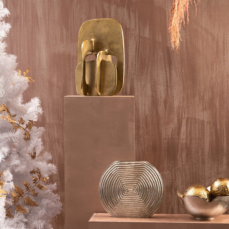Golden abstract sculpture with geometric layers on a matte beige pedestal next to dax silver small vase small vase
