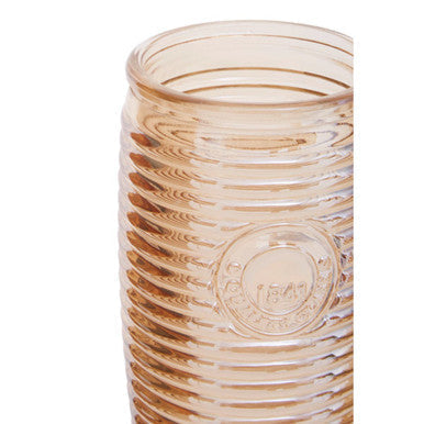 A translucent amber glass vase with vertical ridges and a circular logo near the base next to four gold ribbed glass tumblers