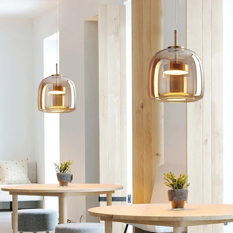 Two decao light pendant lights with amber glass domes and brass accents hanging above wooden tables