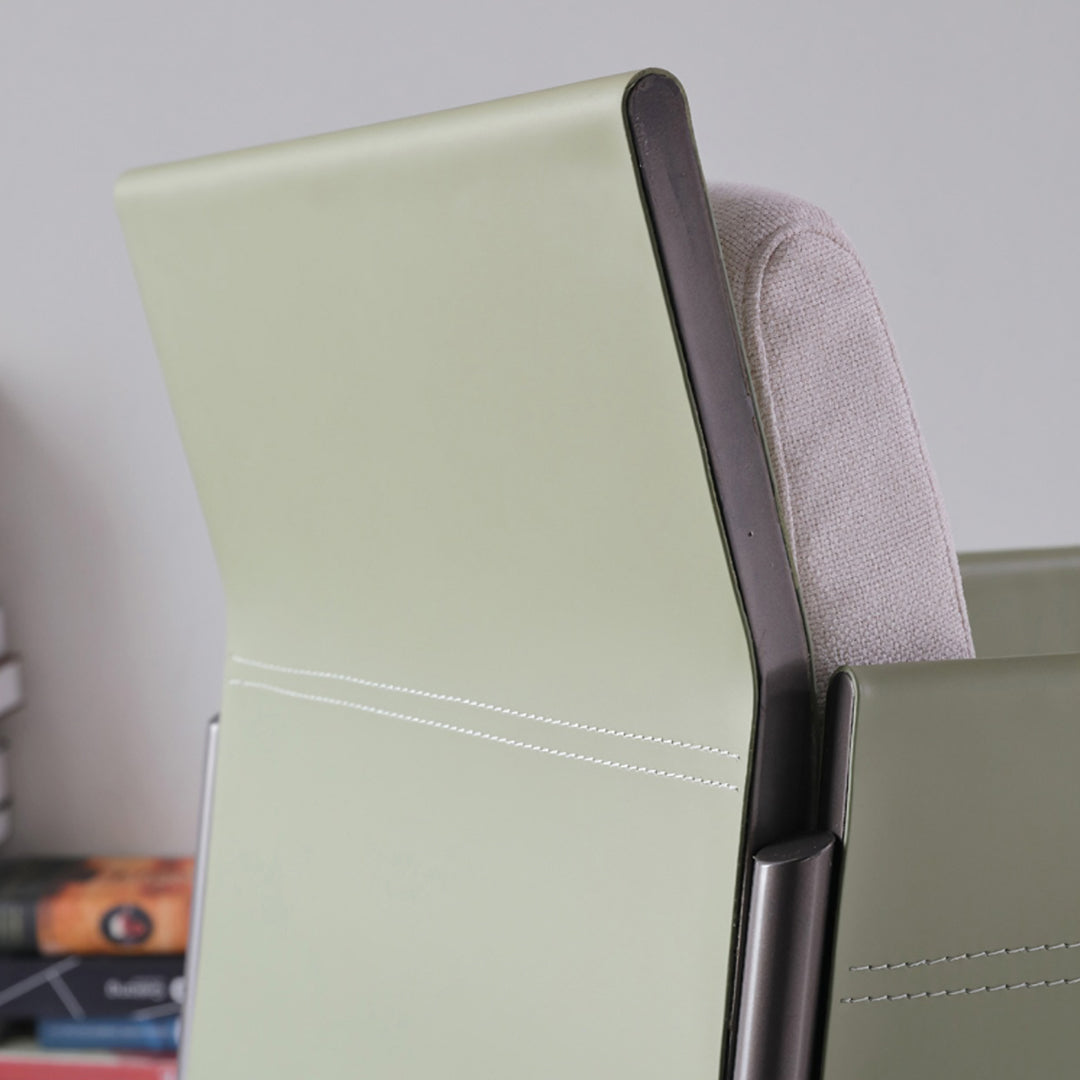 Back of a decker dining chair in sage green leather with white stitching and a dark metal frame for dining use