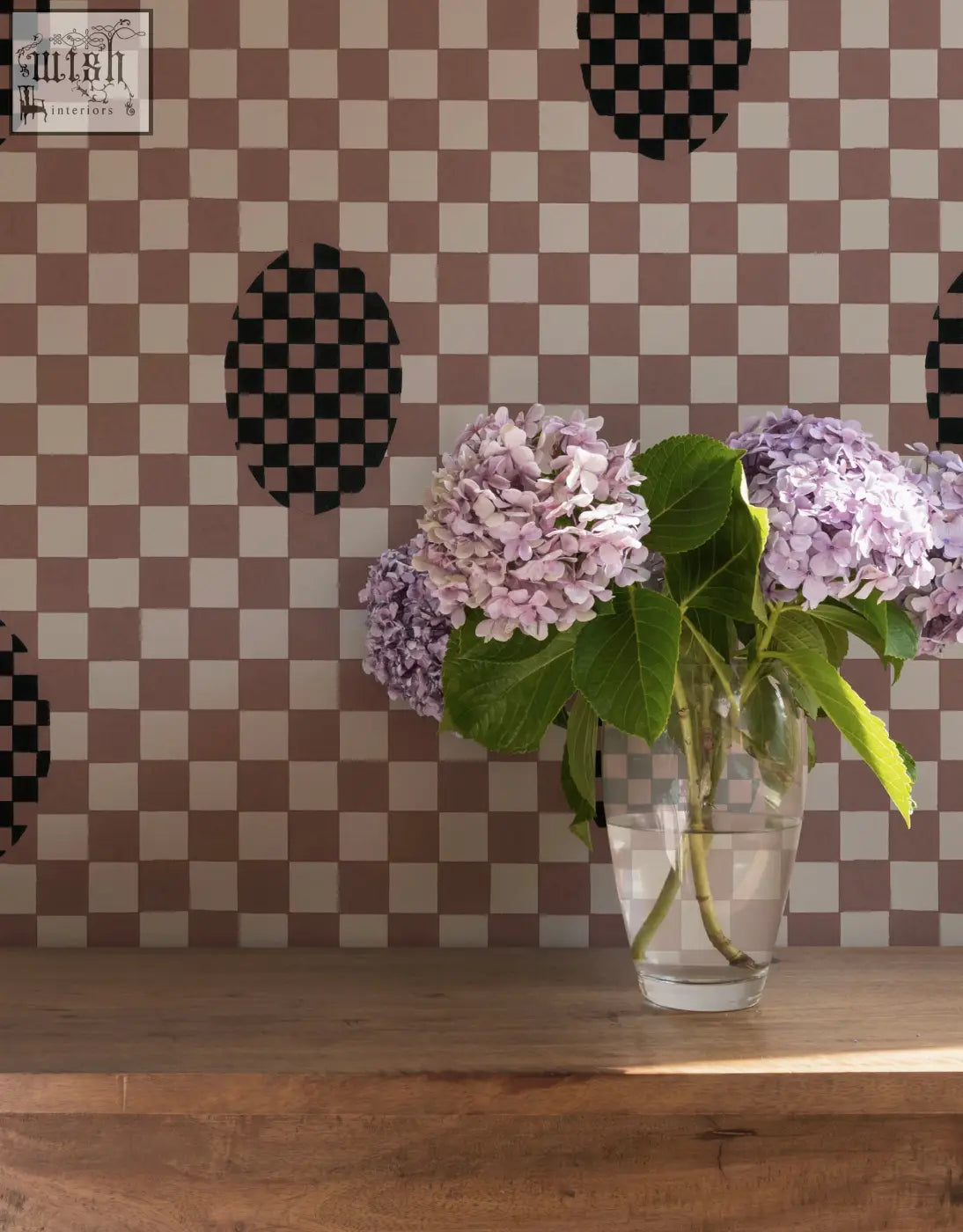 A clear glass vase with light purple hydrangeas in front of deco checkers wallpaper in toasted coco by micaela sharp digital printing
