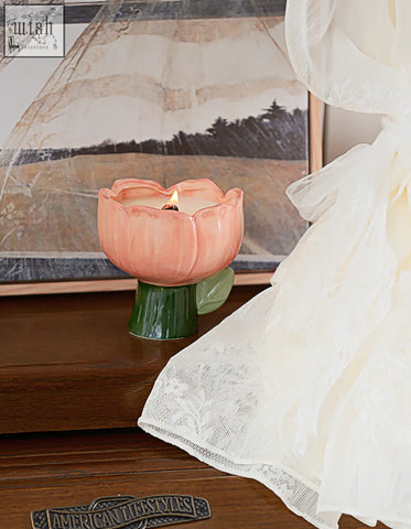 A peach-colored ceramic tulip-shaped delphine scented candle holder with a green stem and lit wax candle inside offers financing options