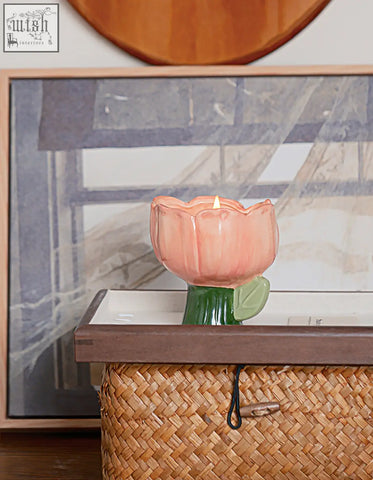 A pink ceramic tulip-shaped delphine scented candle holder with green stem and lit candle offering financing options