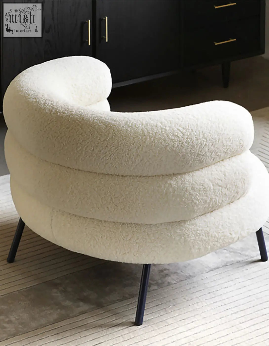 Cream-colored plush demure boucle armchair with modern curved design and black metal legs adds art-deco glamour