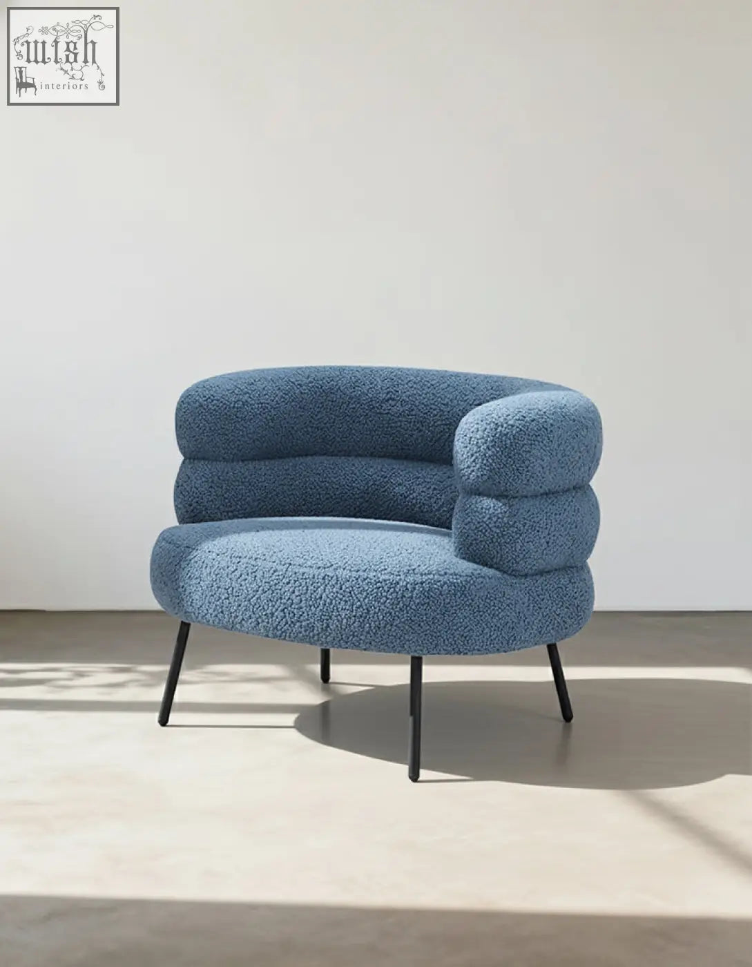 A plush light blue demure boucle armchair with cloud-like design and thin black metal legs adds art-deco glamour