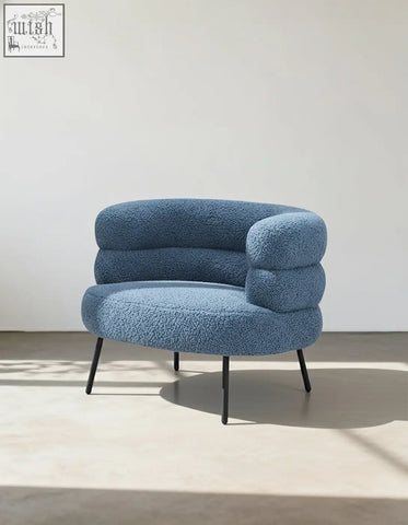 A plush light blue demure boucle armchair with cloud-like design and thin black metal legs adds art-deco glamour
