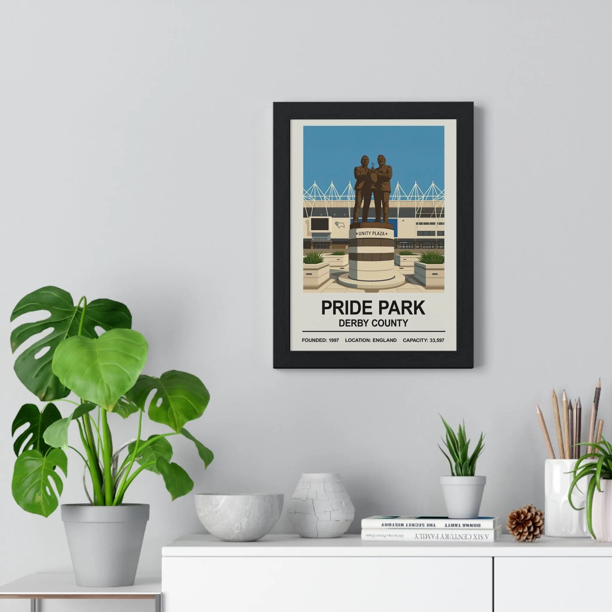 Black-framed derby county pride park stadium print with stylized figures on a pedestal and pride park text