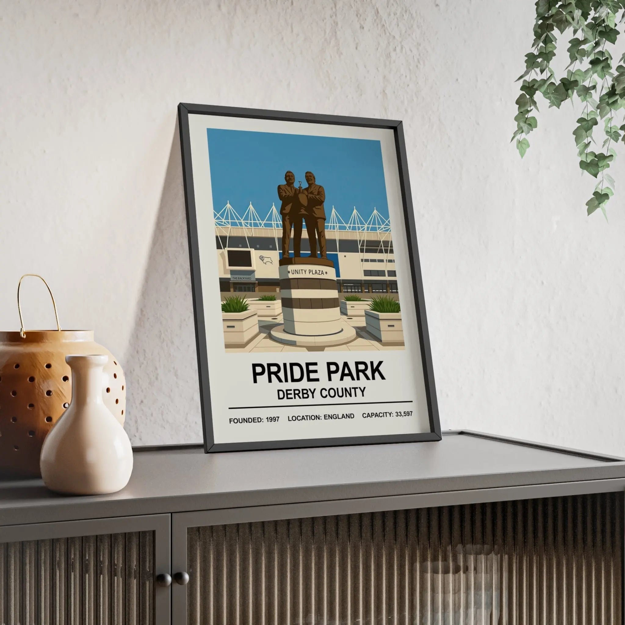 A framed derby county pride park stadium print featuring a stylized illustration with bronze statues and blue sky