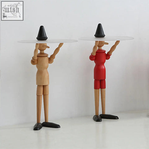 Two solid wood derby pinocchio puppets in natural and red colors with black hats and shoes on a side table