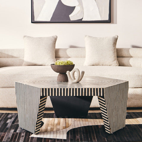 Hexagonal coffee table with black and white stripes and sleek geometric legs next to a textured grey pedestal bowl