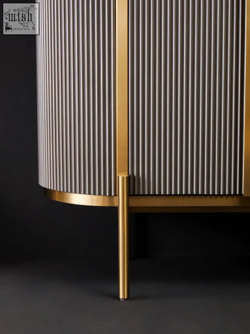Gold-toned cylindrical cabinet with vertical ribs paired with dervio grey four door sideboard featuring black marble top