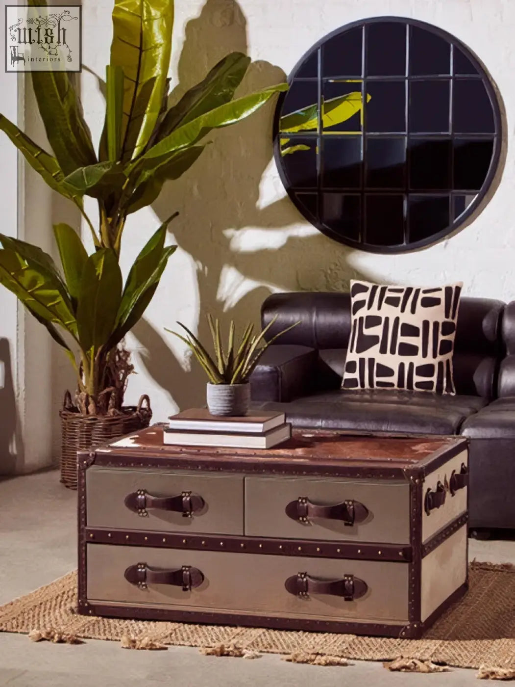 Vintage-style coffee table with distressed metal frame wooden top and black leather accents next to descartes round metal wall mirror
