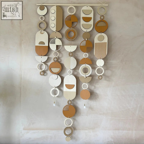 A hand painted geometric wall hanging with layered wooden discs in warm beige cream and terracotta tones