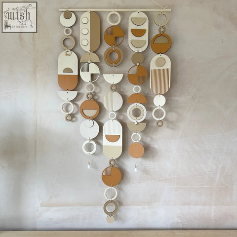 A modern geometric wall hanging with hand painted engraved wooden shapes in earthy beige cream and warm brown tones