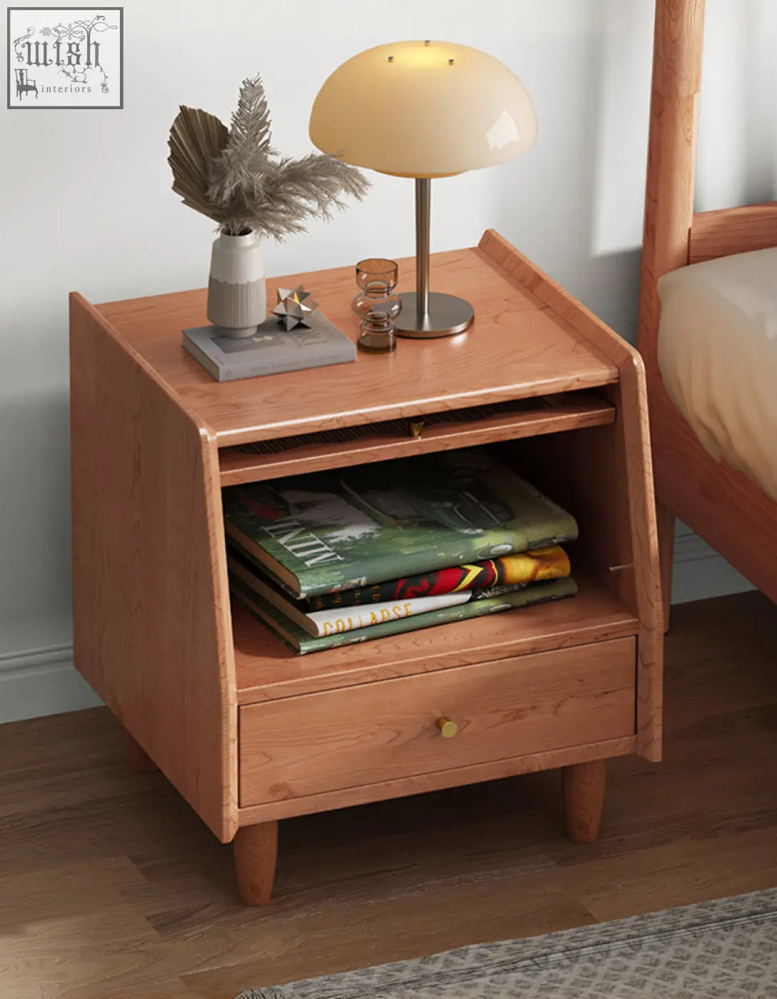 Warm-toned solid wood devin bedside table with curved top, open shelf for magazines, and single drawer with round brass knob
