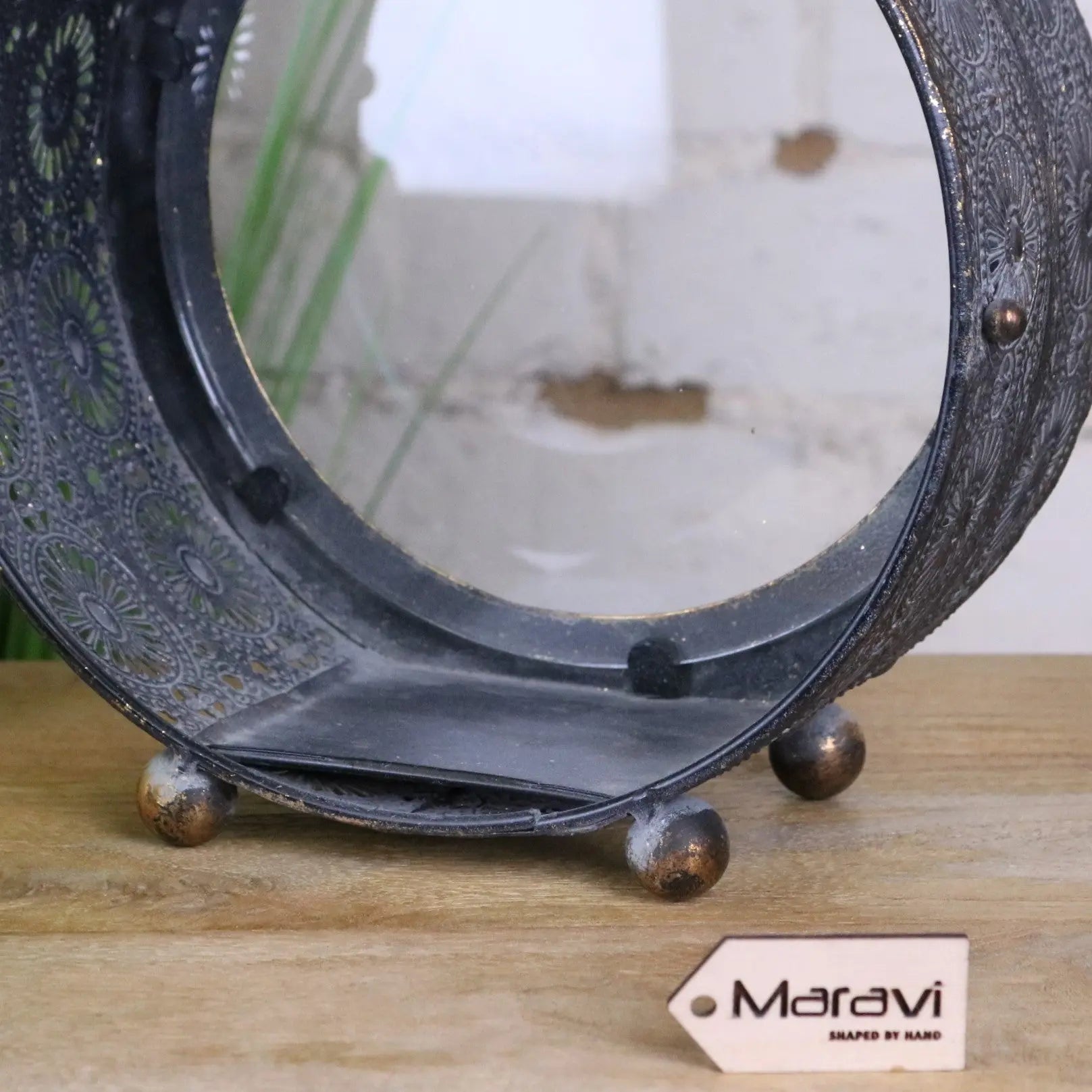 Black ornate metal mirror with floral etchings and brass feet paired with devra vintage style round lantern