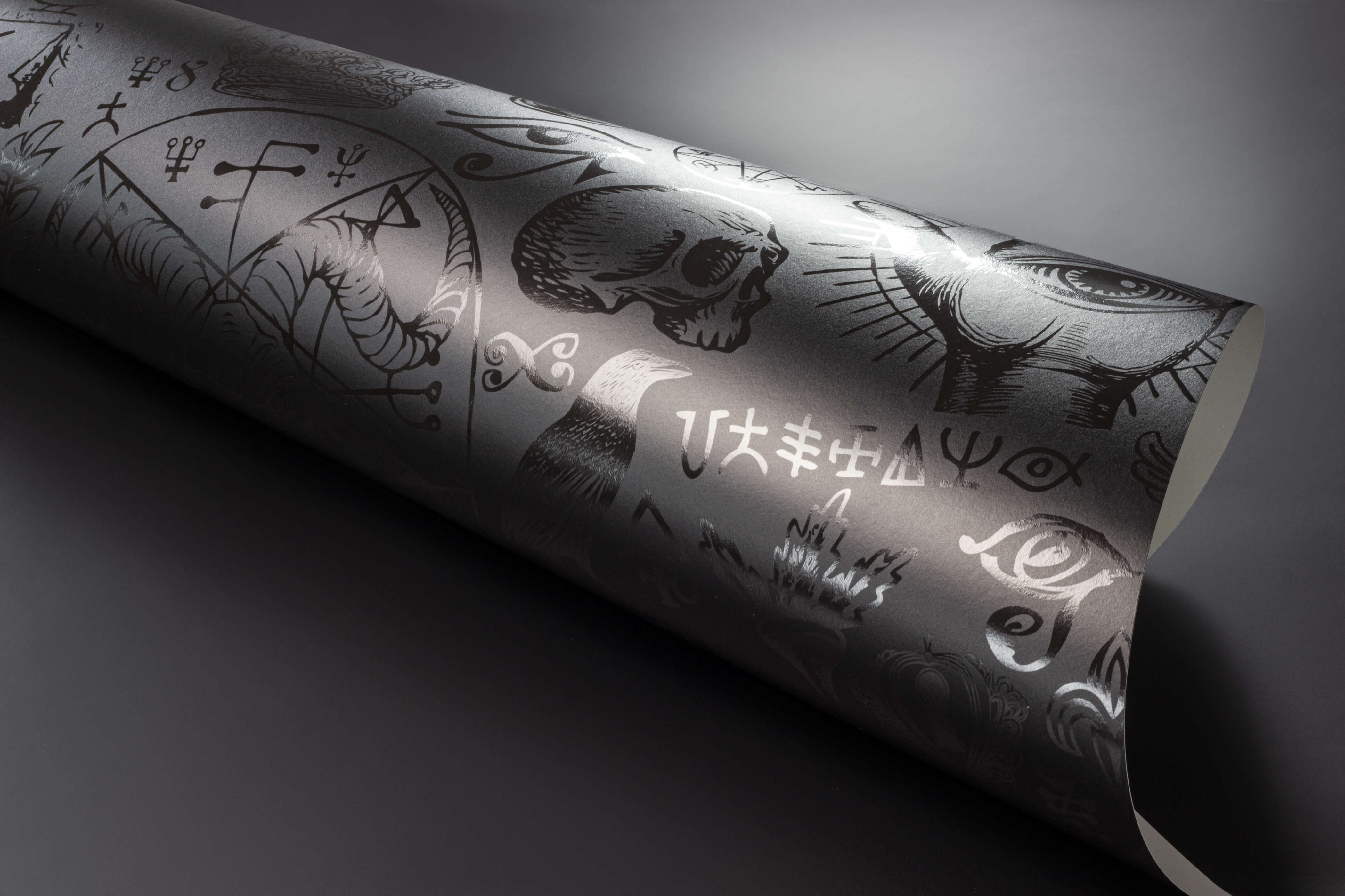 A rolled-up diablo wallpaper in dark gray with intricate black skulls eyes and mystical symbols illustrations