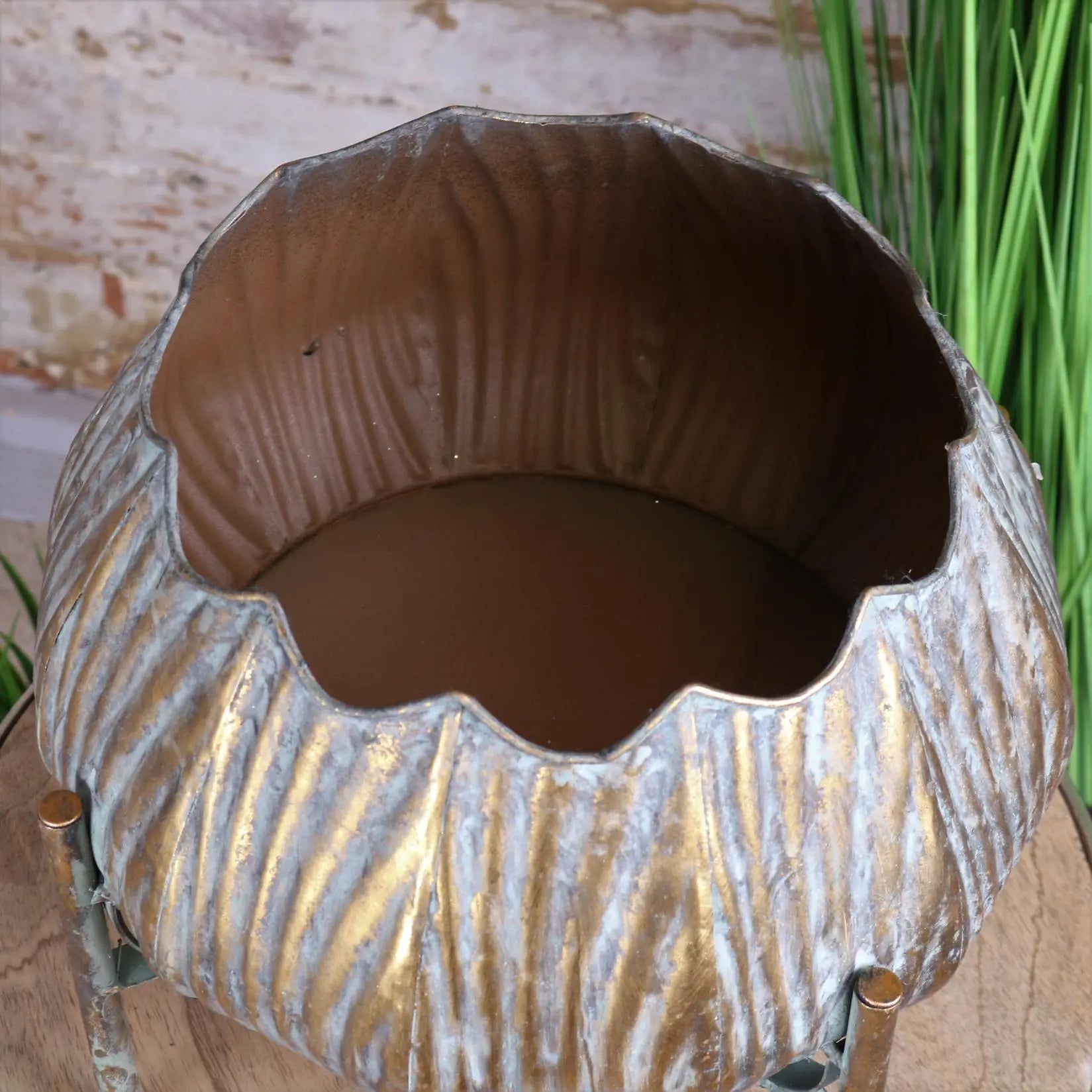 A rustic metallic dimma plant stand with scalloped rim vertical ridges and aged bronze finish for indoor plants