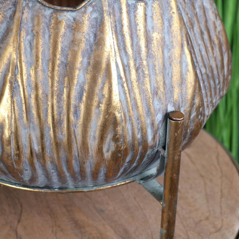 A rustic ribbed metal dimma plant stand pumpkin planter with distressed gold and silver finish for indoor use