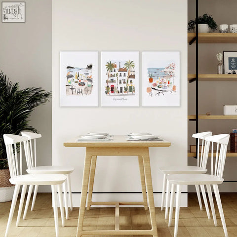 Light wood dining table with slender legs and white chairs shown with amalfi coast dining room wall art set of 3