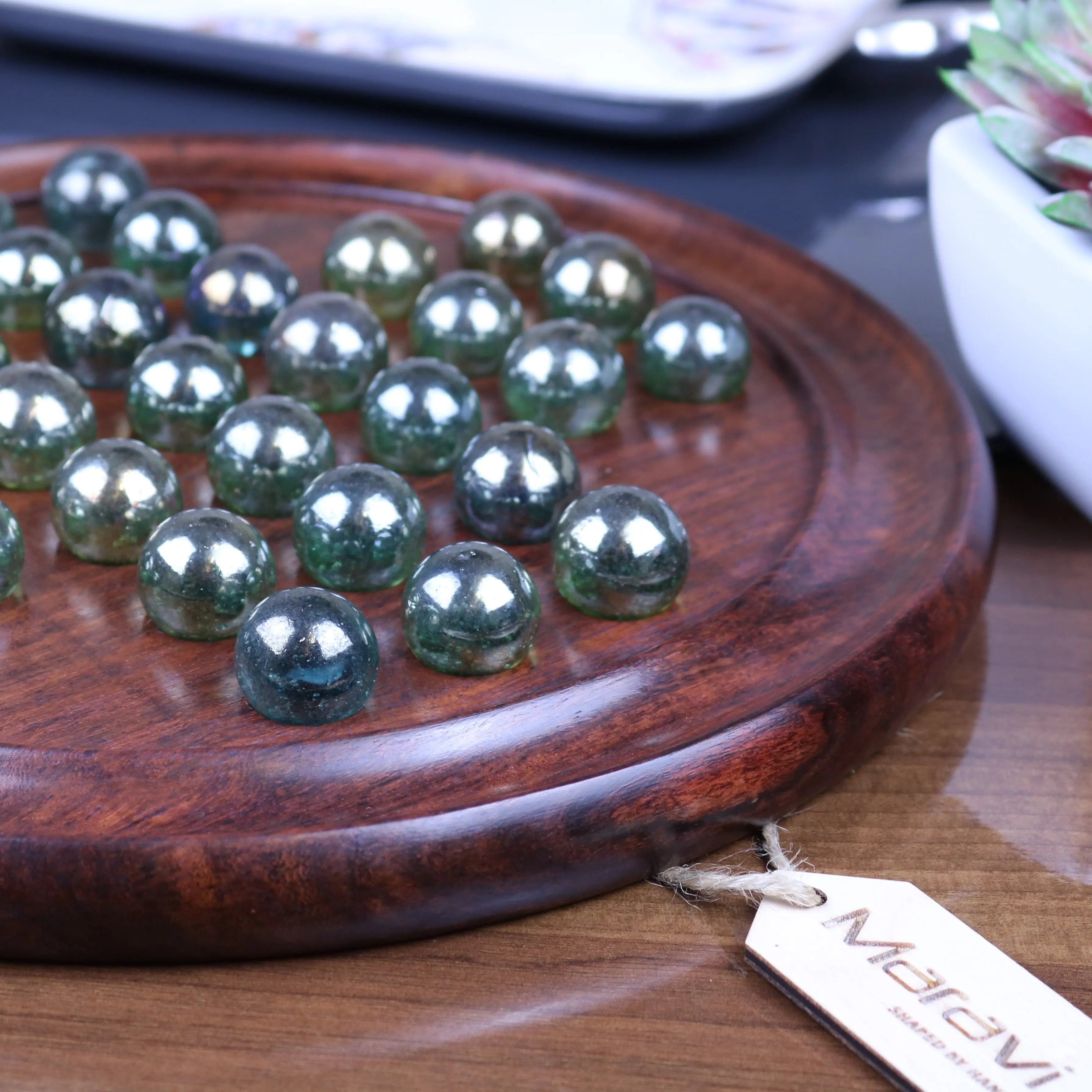 A translucent green glass marble set arranged on a polished dark wood board in the dinod wooden solitaire game set
