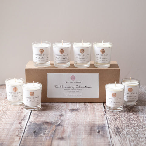 Set of six clear glass candles with white wax and minimalist labels arranged around perfect chaos discovery set box