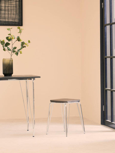 Dark green textured glass vase with slender neck on district chrome metal and elm wood table holding artificial foliage
