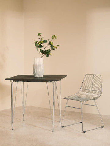 A sleek wireframe chair with chrome finish and geometric mesh design paired with district chrome metal elm wood table