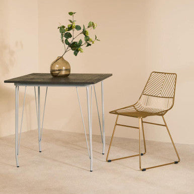 Gold wireframe chair with geometric pattern and slender legs paired with grey metal and elm wood dining table