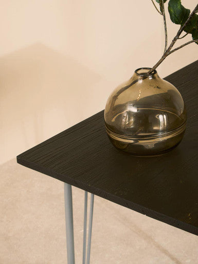 A sleek amber glass vase on a grey metal and elm wood dining table perfect for wood dining spaces
