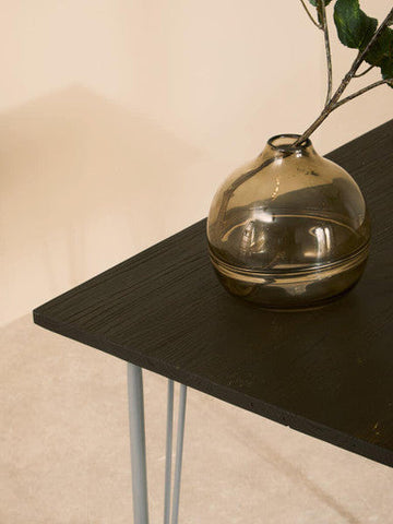 A sleek amber glass vase on a grey metal and elm wood dining table perfect for wood dining spaces