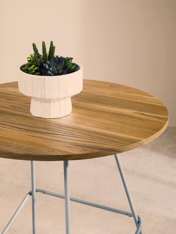 White geometric planter with green and dark blue succulents on a district grey metal and elm wood round dining table