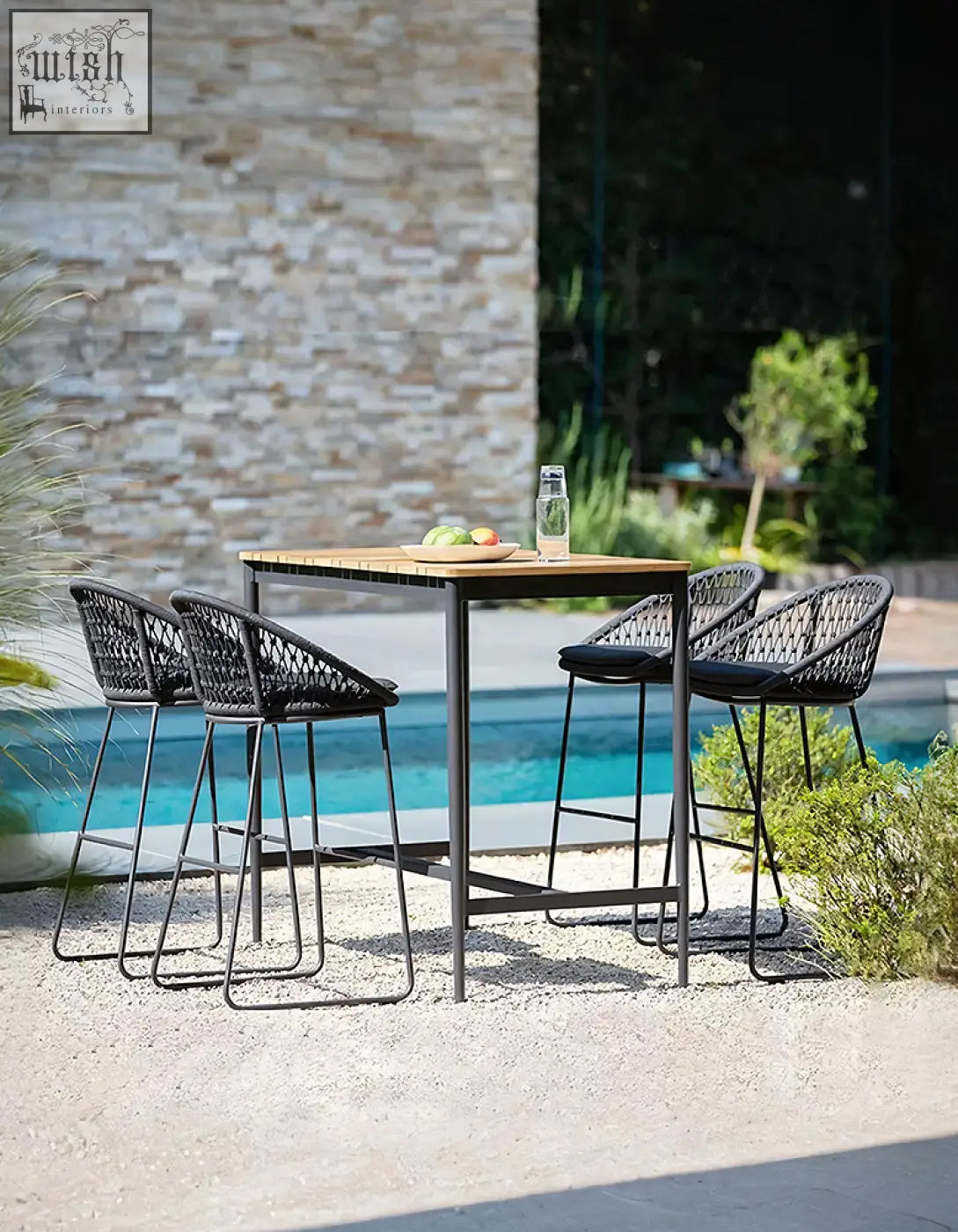 Black woven mesh bar stools with black cushions around a wooden dmitry outdoor garden table on a patio