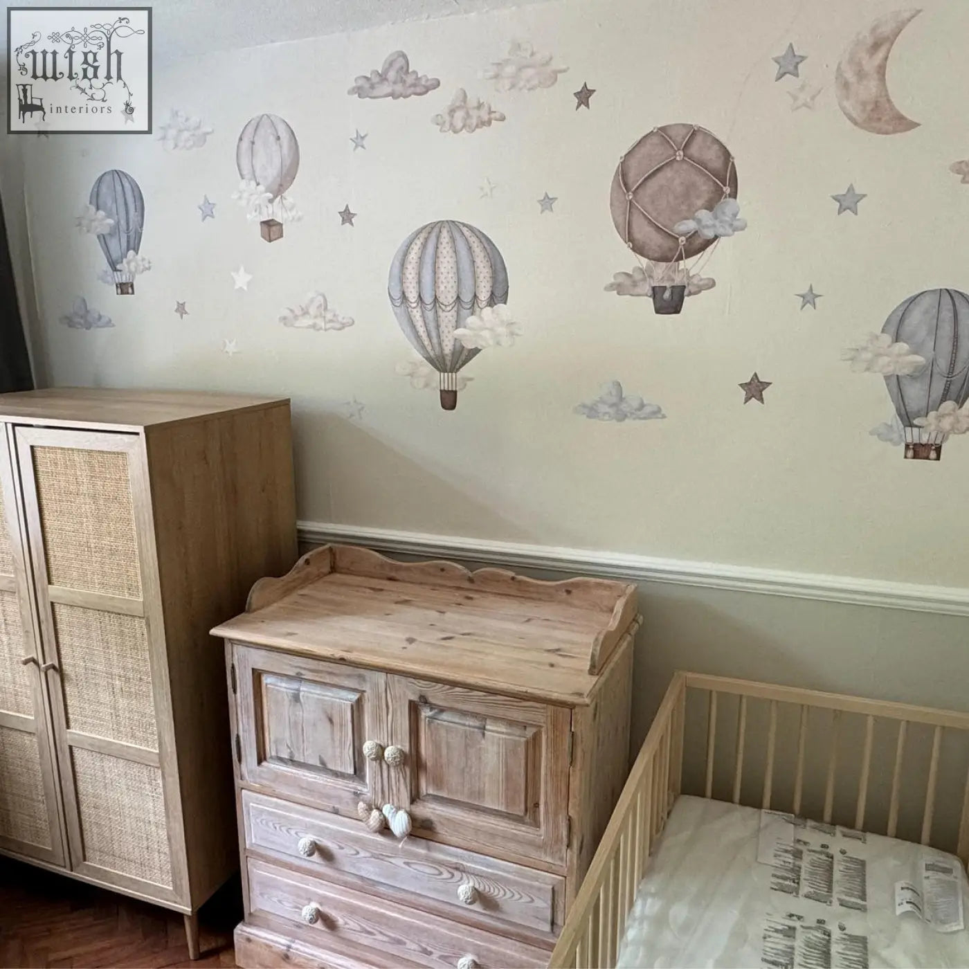 Light brown wooden changing table with scalloped top and heart handles paired with dreamy hot air wall decals