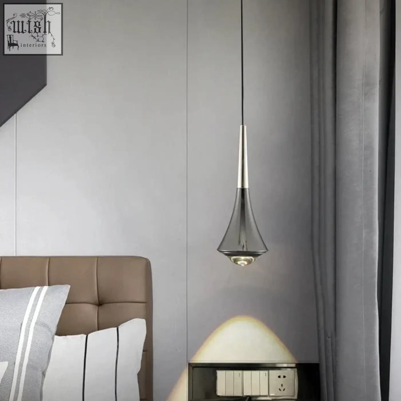A sleek dropping pendant light with metallic silver stem and transparent glass shade tapered to a pointed tip