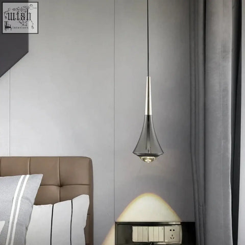 A sleek dropping pendant light with metallic silver stem and transparent glass shade tapered to a pointed tip