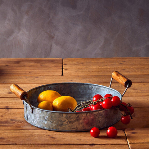 Galvanised metal serving tray with wooden handles holding lemons and cherry tomatoes from three round galvanised set