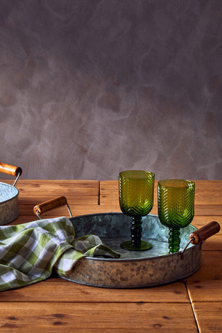Green ribbed wine glasses with dark green stems on a rustic three round galvanised steel tray with wooden handles