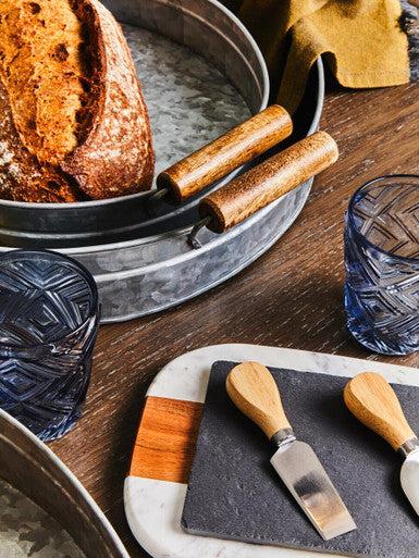 Wooden-handled cheese knives on marble and slate board with three round galvanised steel trays for serving
